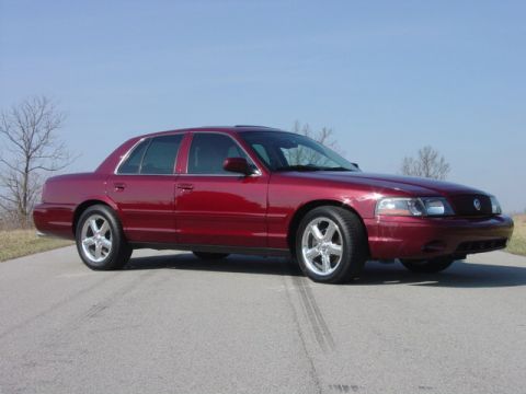 1998 Ford Crown Victoria - Clean side-profile shot of a dark red Mercury Marauder sedan parked on a paved road under a bright blue sky.