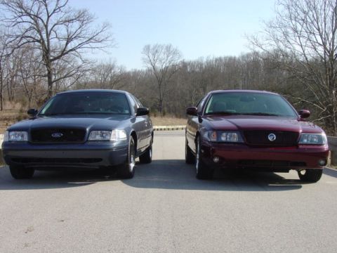 1998 Ford Crown Victoria - gray Ford Crown Victoria beside a maroon Mercury Marauder, both shown head-on in a parking lot with bare winter trees behind.