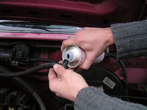 1994 Ford Bronco - A mechanic pours fluid from a can into a hose in the engine bay of a 1994 Ford Bronco.
