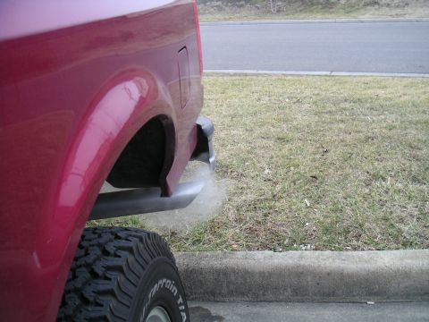 1994 Ford Bronco - Rear view of a red SUV, showing the quarter panel, tire, and exhaust pipe with visible smoke.