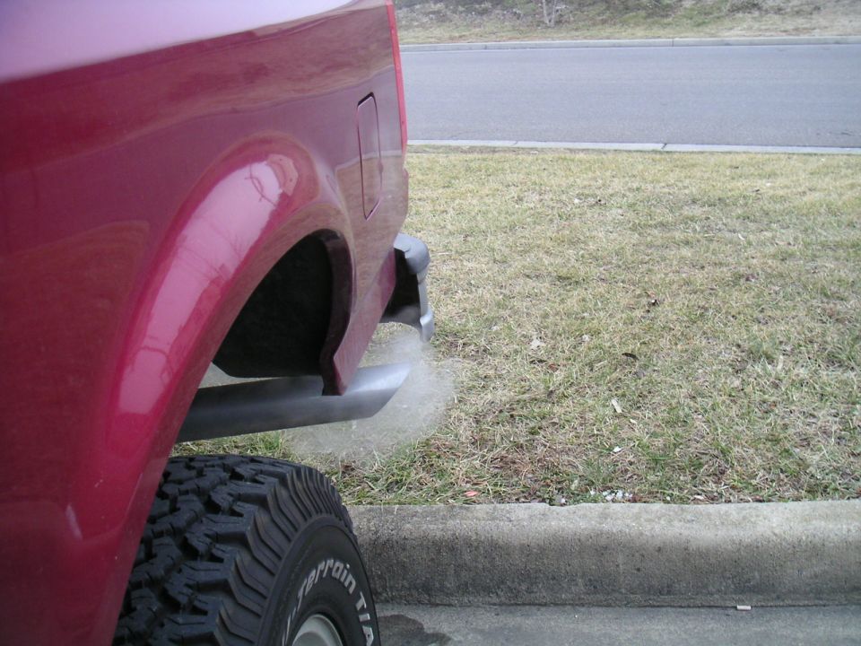 Red SUV's rear quarter panel, tire, and exhaust pipe emitting smoke. The body style suggests a 1992 model