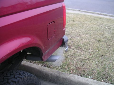 1994 Ford Bronco - A red pickup truck's exhaust pipe is visible, emitting a cloud of smoke near a curb and grassy area.