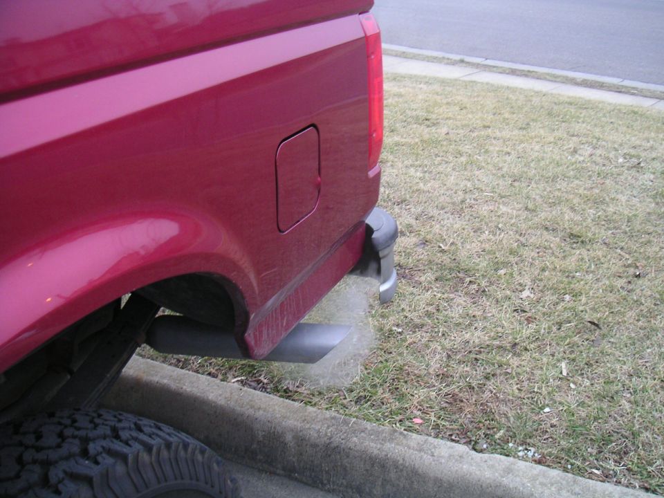 Red pickup truck's rear quarter panel, tire, and exhaust pipe emitting smoke