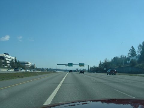1999 Ford Crown Victoria - A view from a vehicle traveling on a highway, passing by office buildings and other cars on a clear day.
