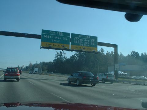 1999 Ford Crown Victoria - A highway scene shows traffic moving under overhead exit signs indicating "11B 148th Ave SE" and "11A 150th Ave SE".