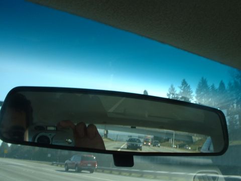 1999 Ford Crown Victoria - A view of highway traffic is seen in the rearview mirror, including a red SUV and other vehicles.