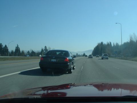 1999 Ford Crown Victoria - A black sedan drives on the highway under a clear blue sky.