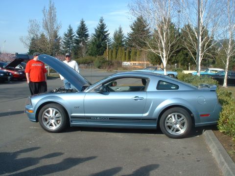 1999 Ford Crown Victoria - A light blue Ford Mustang GT 500 is parked with its hood open, while other vehicles are visible in the background.