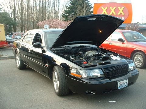 1999 Ford Crown Victoria - A black 2003 Ford Crown Victoria is displayed with its hood open, revealing the engine compartment, while another Crown Victoria is parked…