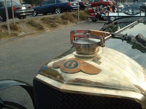 1999 Ford Crown Victoria - A close-up view of a vintage Bentley's winged B hood ornament and a chrome fuel cap.