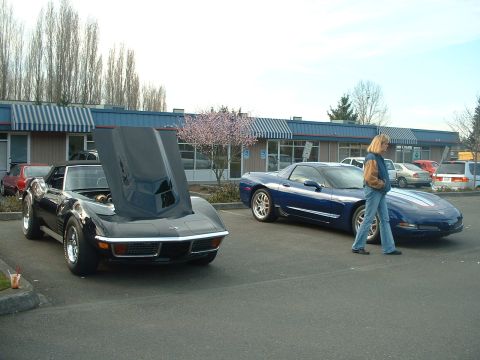 1999 Ford Crown Victoria - Two Corvettes, one classic with its hood up and a modern one, are parked outside a building.