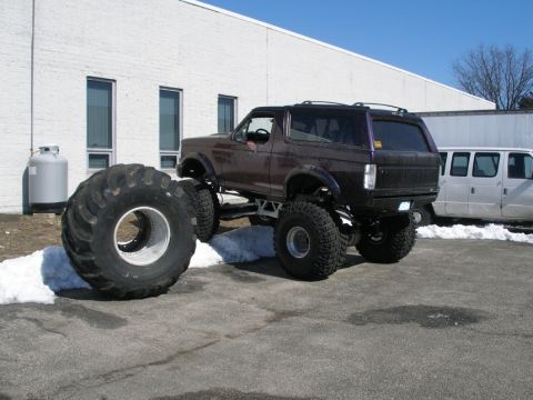 1994 Ford Bronco - This modified Ford Bronco sits high off the ground with its large tires, one of which is detached and resting beside the vehicle.