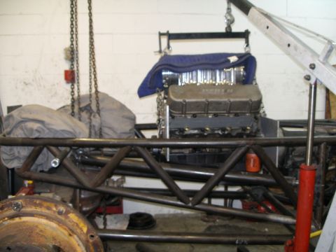 1994 Ford Bronco - An engine is suspended by chains and a hoist, positioned above a custom-built tube frame chassis in a workshop.