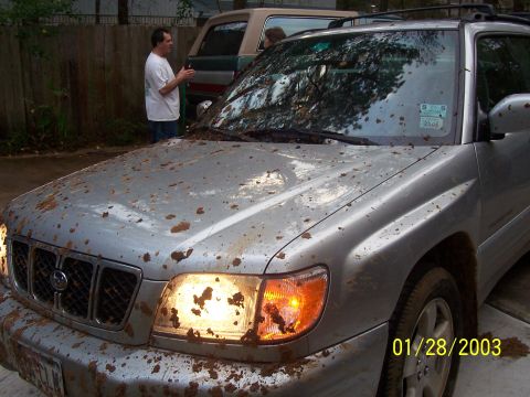 1989 Ford Bronco - A silver SUV is covered in mud, with its headlights illuminated.