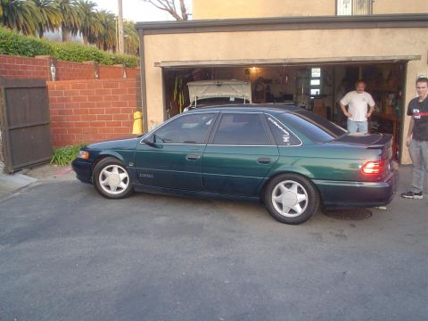 1993 Ford Taurus - A green 1993 Ford Taurus is parked outside a garage with its doors open.