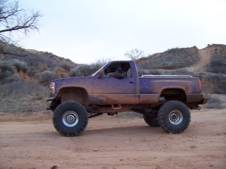 Mud-covered purple pickup truck with large tires driving on a dirt road