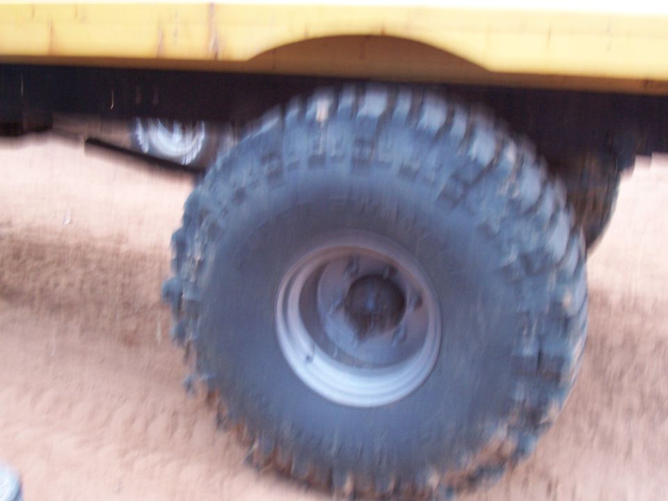 Close-up of a large, knobby off-road tire and part of a yellow vehicle's frame