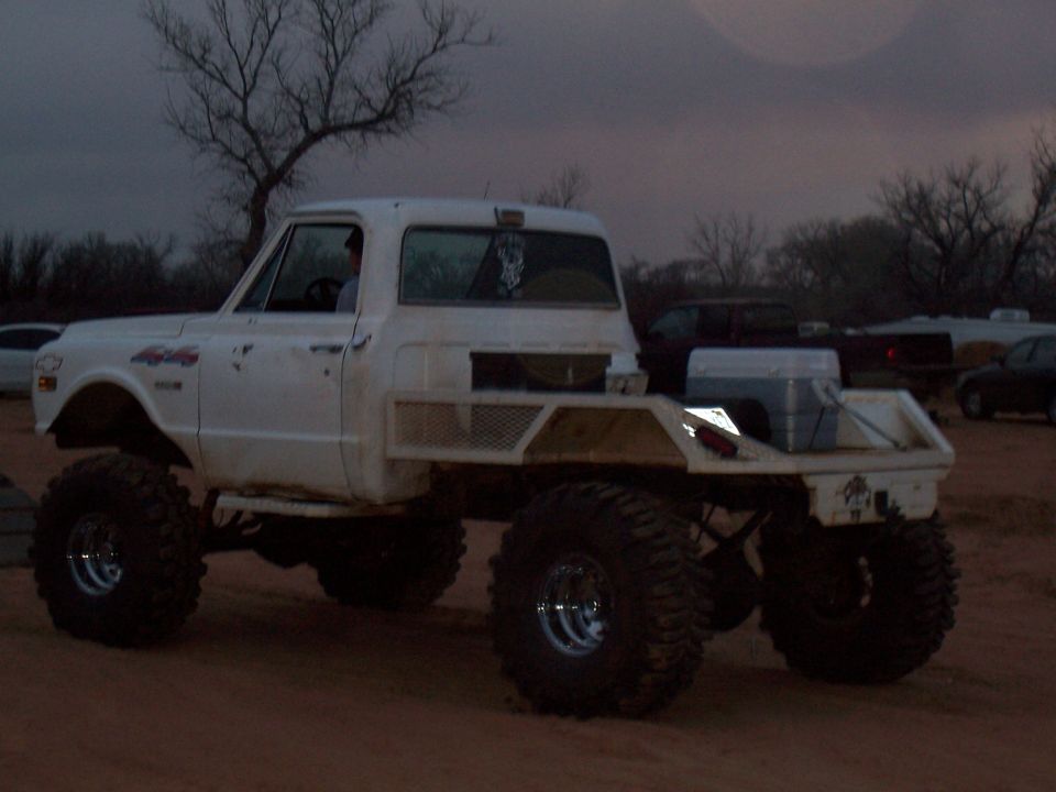 White pickup truck with large tires and a flatbed, parked outdoors