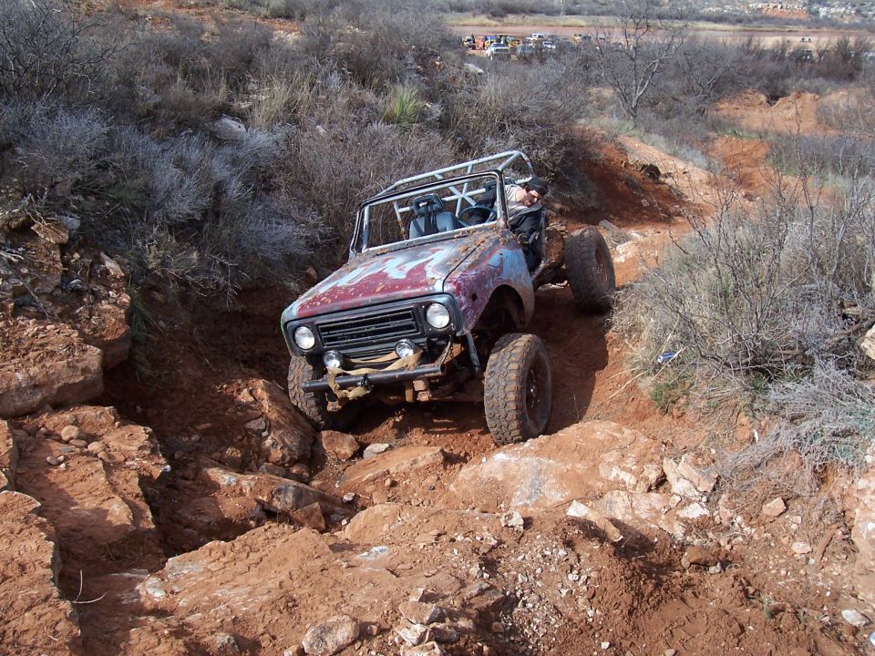 Modified off-road buggy with roll cage navigating a steep, rocky trail. Red and blue paint is heavily weathered