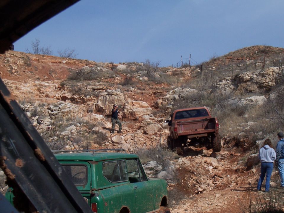 Green SUV and a rusty brown pickup truck navigate a steep, rocky terrain under a clear blue sky