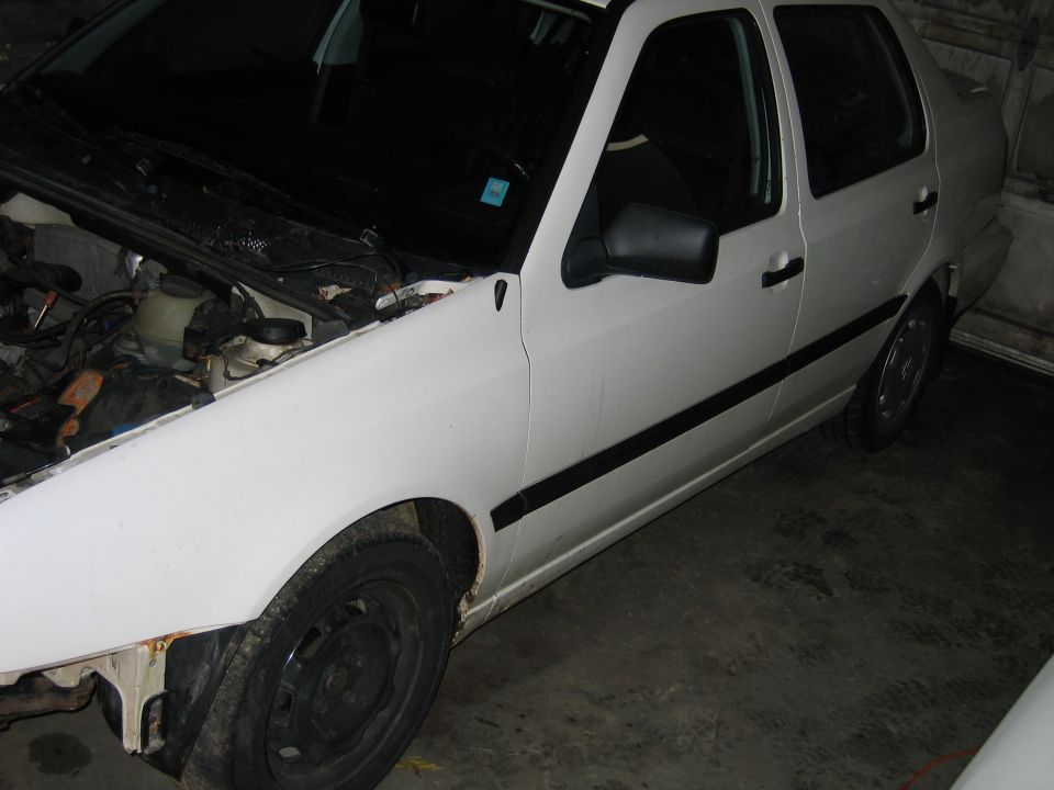 White sedan, hood open, showing engine components. Black trim along doors, black side mirror. Some rust on front fender