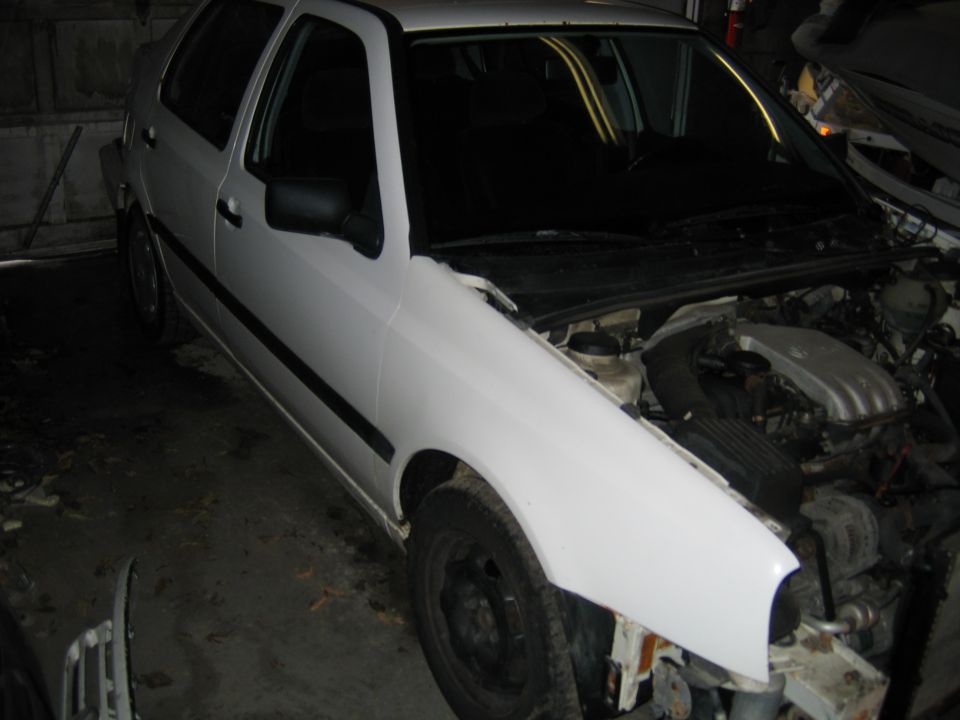White hatchback with hood open, showing engine components. Front bumper is missing