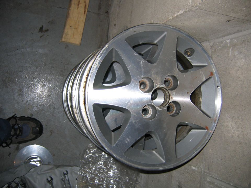 Stack of five silver alloy wheels with five spokes, some showing wear and corrosion
