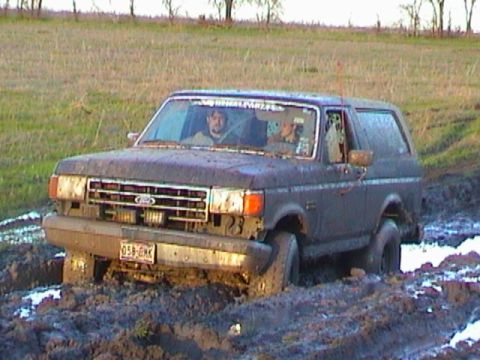 1989 Ford Bronco - This 1989 Ford Bronco is stuck deep in the mud, with two occupants visible inside.
