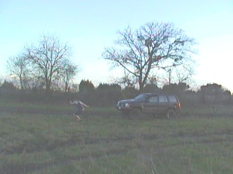 1989 Ford Bronco - A person runs in a field next to a Jeep Grand Cherokee under a clear sky with bare trees.