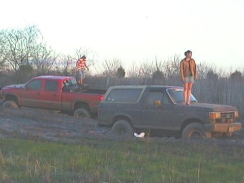 1989 Ford Bronco - Two trucks are stuck in the mud, with people standing on top of each vehicle.
