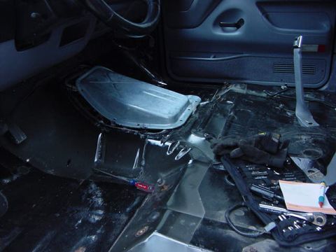 1995 Ford Bronco - The interior floor of a vehicle is shown with the carpet and some panels removed, revealing the metal structure beneath.