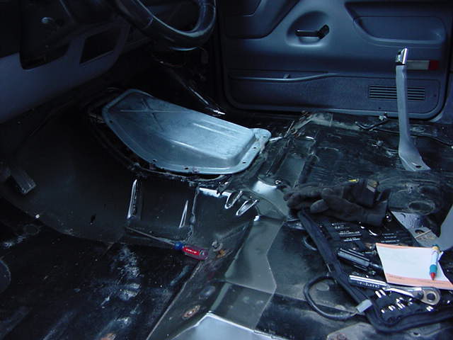 Interior floor of a vehicle with parts removed, showing the transmission tunnel and tools on the floor