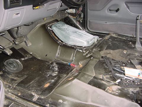 1995 Ford Bronco - The interior floor of a vehicle is shown with the carpet removed, revealing tools and a pair of gloves.
