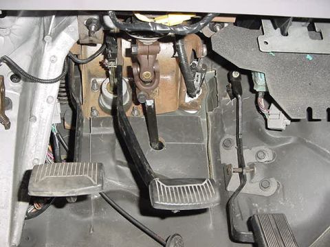 1995 Ford Bronco - The footwell of a vehicle shows the brake, clutch, and gas pedals along with associated wiring and linkages.