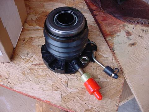 1995 Ford Bronco - A clutch slave cylinder, likely for a vehicle, is shown on a wooden surface next to a cardboard box.