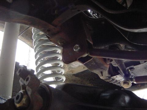 1995 Ford Bronco - Underside view of suspension components, including a white coil spring and various metal brackets and bars.