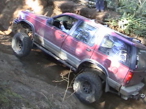 1994 Ford Explorer - A red SUV is shown off-roading on a steep dirt hill, demonstrating its off-road capabilities.