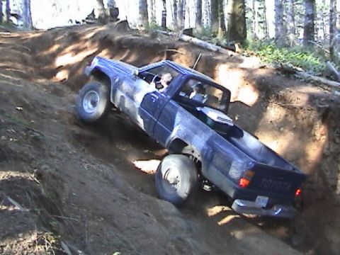 1994 Ford Explorer - A blue Toyota pickup truck navigates a challenging off-road trail on a sunny day.