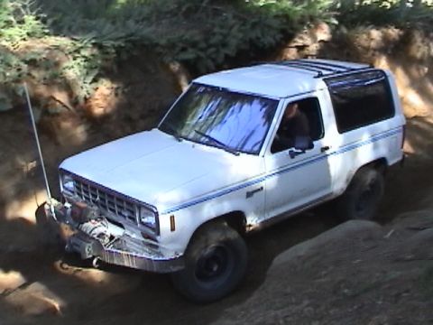 1994 Ford Explorer - This white Ford Bronco II is shown off-roading on a dirt path with trees in the background.