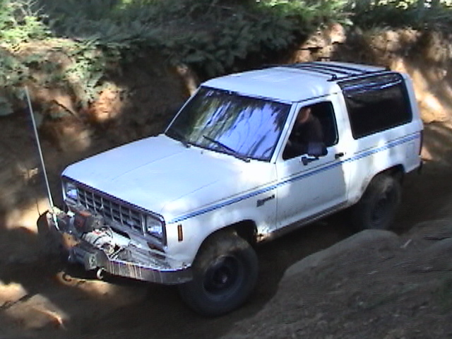 White Ford Bronco II with blue pinstripes navigating a dirt trail, front winch visible