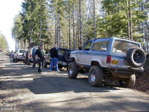 1994 Ford Explorer - A group of off-road SUVs are parked on a dirt road in a wooded area.