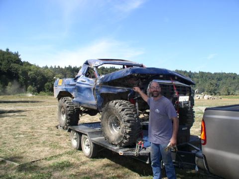 1979 Ford Bronco - Man poses with a severely damaged 1979 Ford Bronco on a trailer, ready for off-road use.