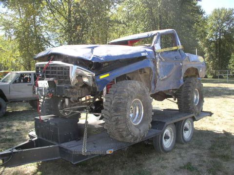 1979 Ford Bronco - A heavily modified pickup truck with oversized tires is loaded onto a trailer.