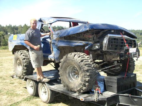 1979 Ford Bronco - A heavily damaged blue 1979 Ford Bronco is loaded onto a trailer, with a man standing beside it.