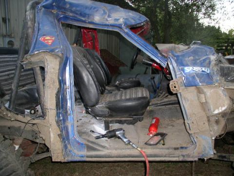 1979 Ford Bronco - Heavily damaged blue pickup truck interior, showing torn seats and bent body panels. Superman logo is visible.