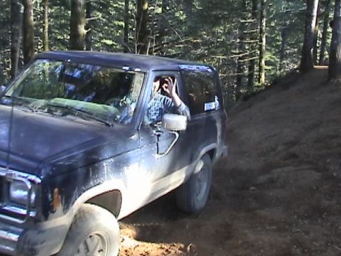 1994 Ford Explorer - A driver signals from inside a dark blue SUV as it navigates a wooded trail.