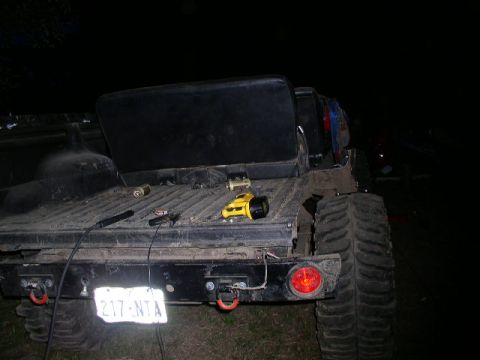 1979 Ford Bronco - The rear of a heavily modified truck is shown at night, with a license plate and large off-road tires visible.