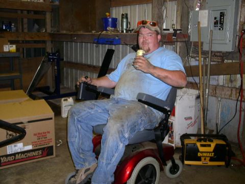 1979 Ford Bronco - Man relaxes in a mobility scooter in a garage, holding a beverage. Various items are stored around him.