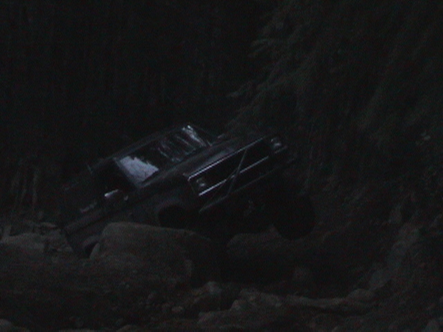 Dark SUV driving over rocks on a trail at night