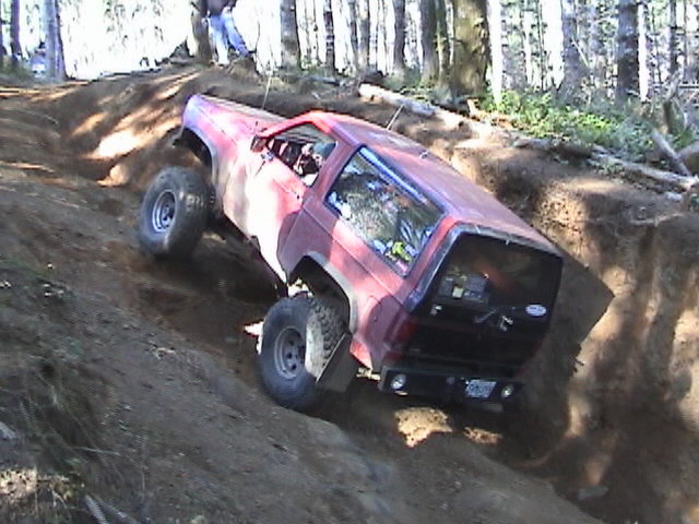 Red SUV with large tires on a steep dirt incline, front wheel lifted